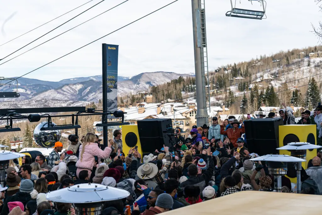 People dancing in front of a DJ booth next to Fanny Hill at Snowmass Ski Area during spring in Snowmass, Colorado.