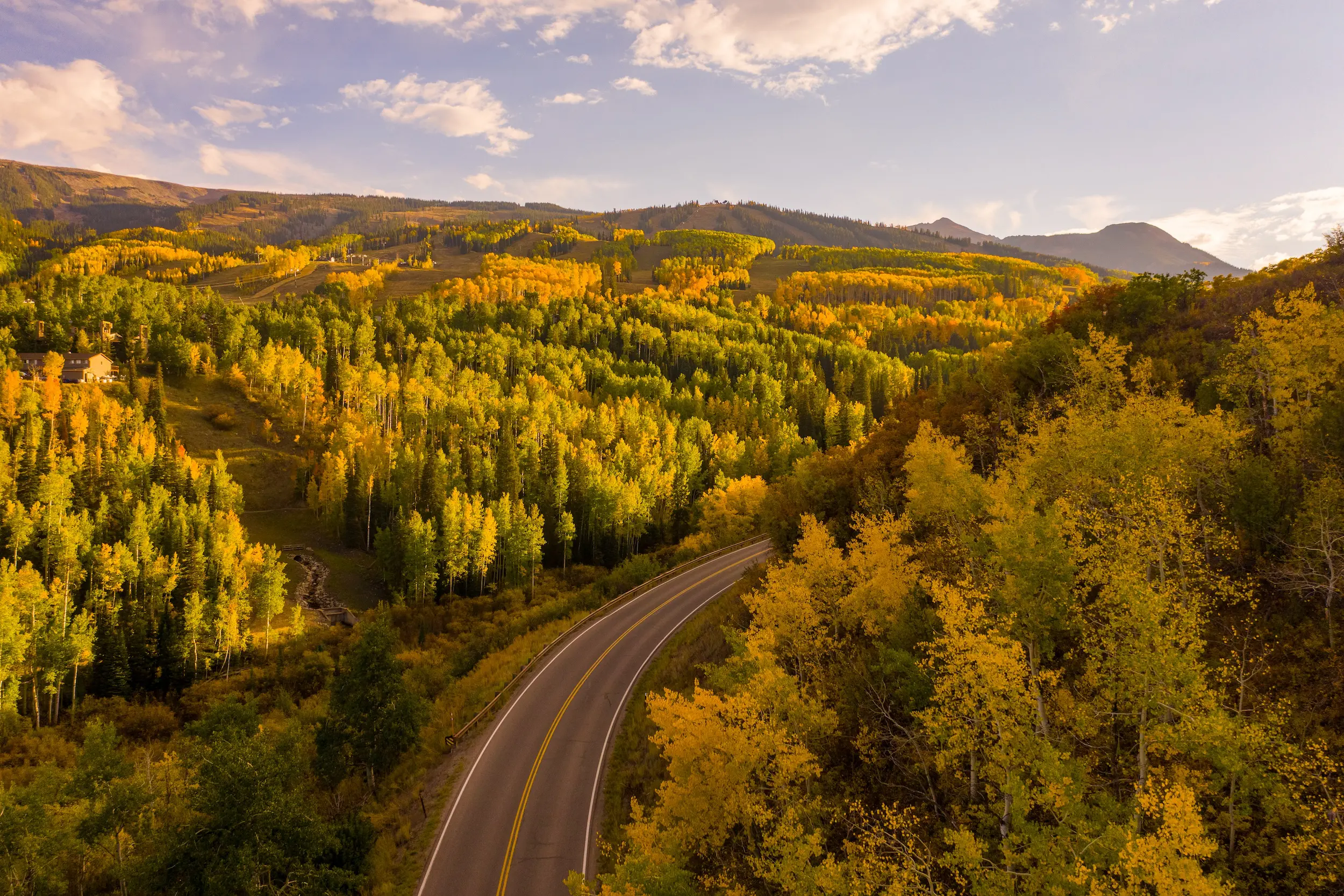 Colorado family vacation idea showing a road cutting through a mountain landscape dotted in yellow and green leaves