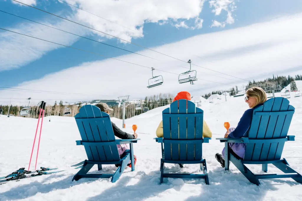 Three women enjoy a sunny après on their winter trip in Snowmass, wearing sunglasses and hats. 