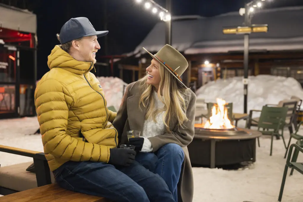 A couple enjoys a cozy outdoor fireside après at The Cabin on a winter trip in Snowmass. 