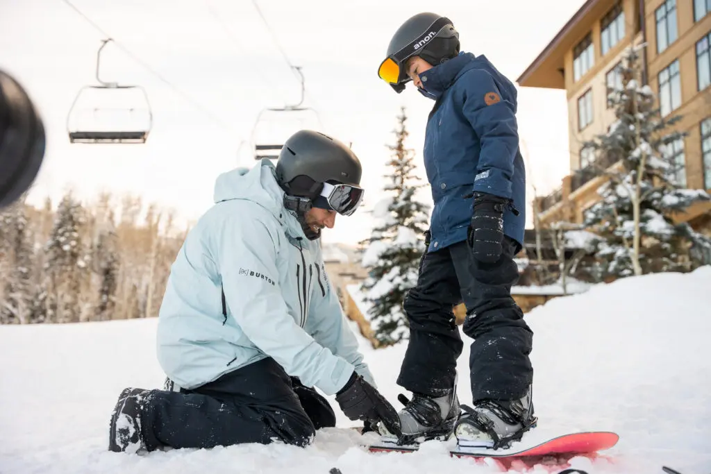 A dad helps his son get his ski gear on during a winter trip to Snowmass.