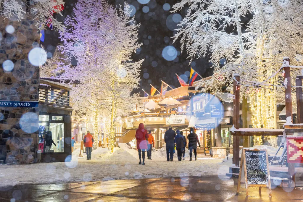 People stroll Snowmass Mall with snowy trees and twinkle lights at nighttime.