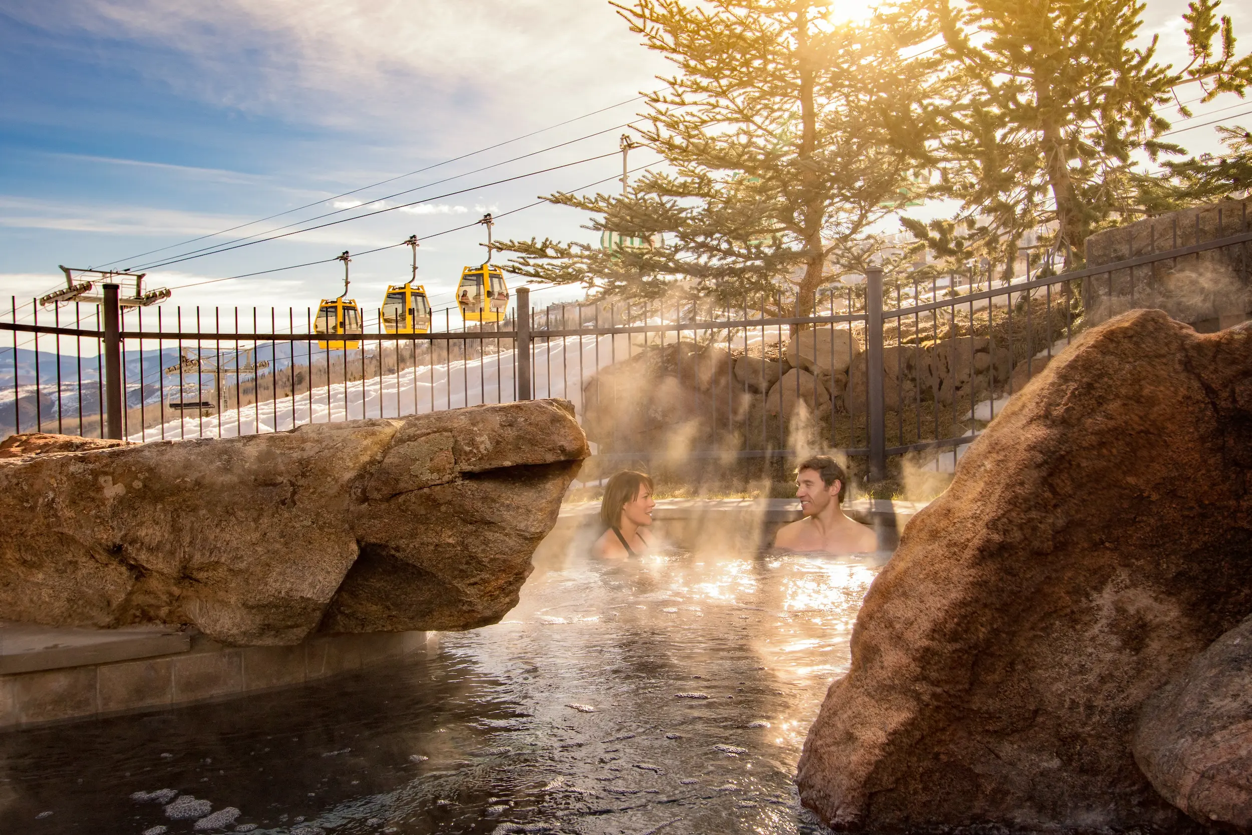couple sitting in a steaming hot tub with gondolas behind them at their ski in ski out lodging