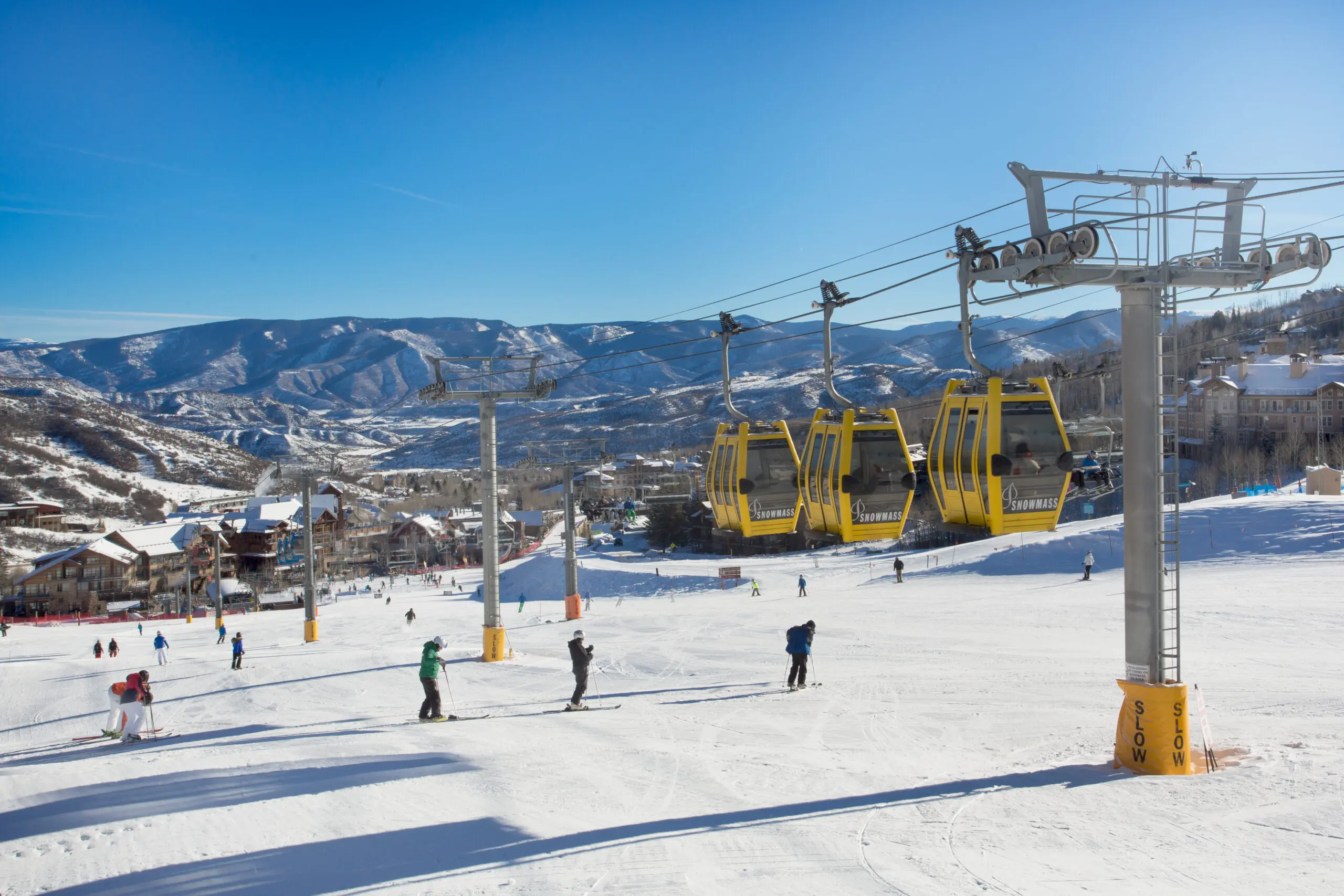 people skiing and snowboarding on a clear blue sky day where you can see ski-in ski-out lodging lining the sides of the run