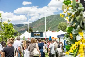 Crowd attends the Food & Wine Classic in Aspen under a blue summer sky with yellow flowers at Wagner Park.