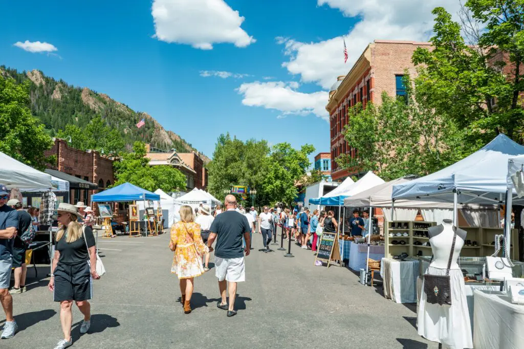 People walk through downtown Aspen among tents with farmers market vendors in the summertime.