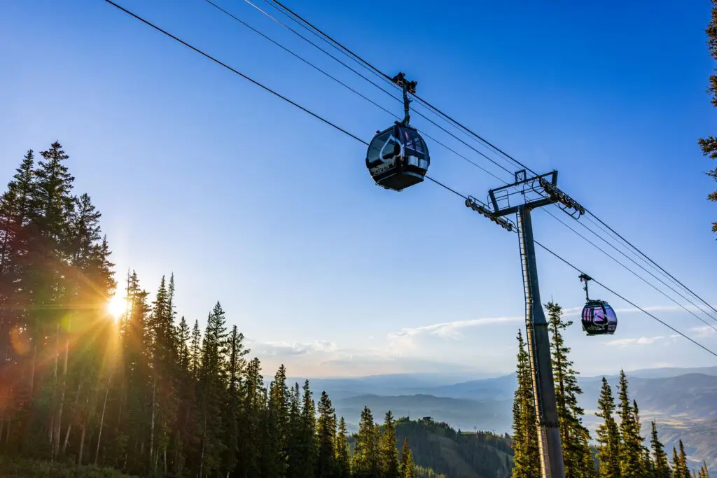 Aspen Mountain gondola cabs halfway up Aspen Mountain with a sunbeam coming through the evergreen trees.