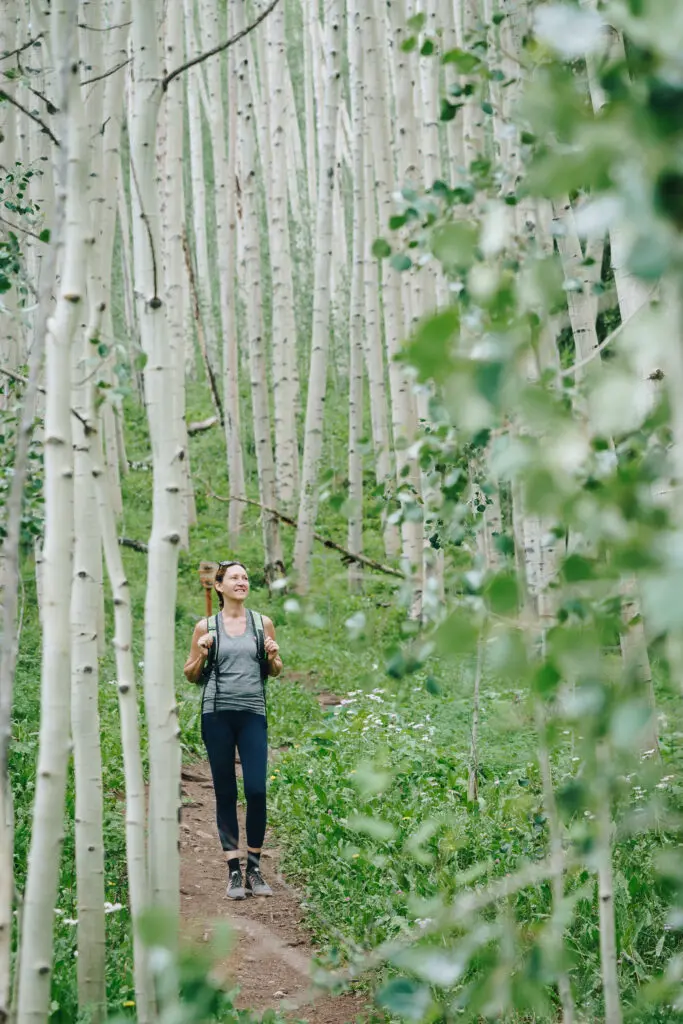 Woman walking through a dense green aspen grove in the summer.