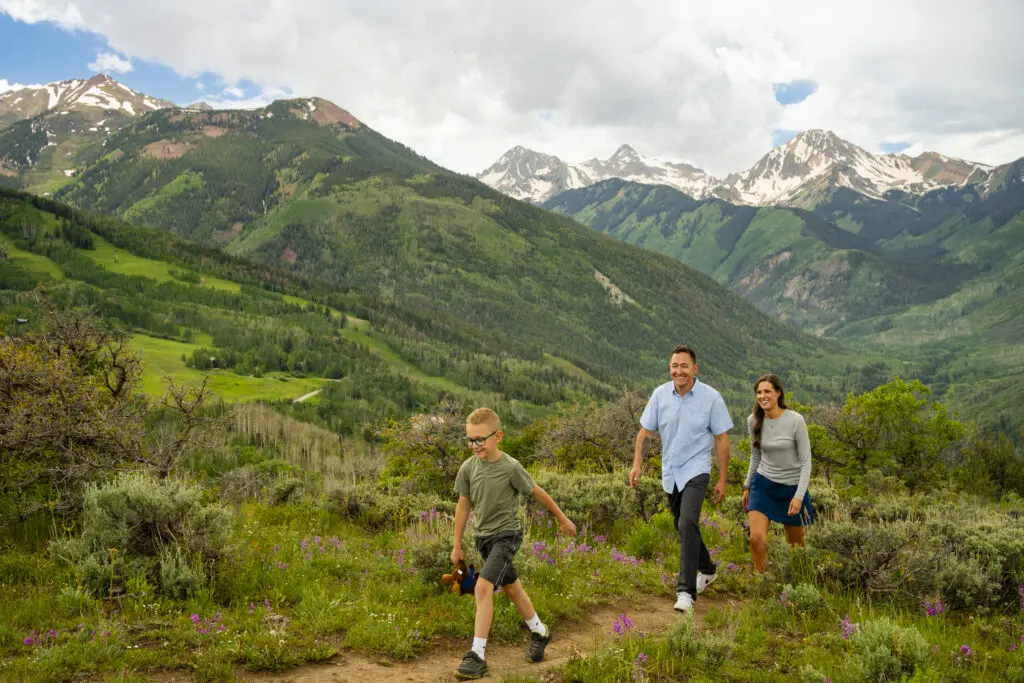 Parents and their young son hike along Rim Trail with Mt. Daly in the background in the summer.