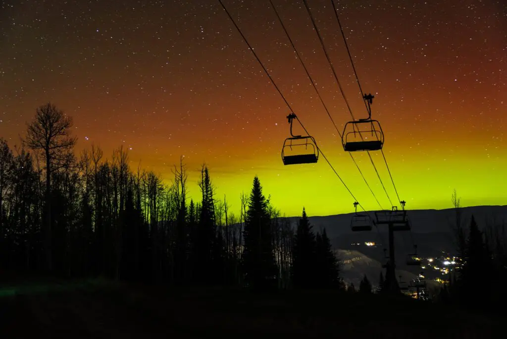 Aurora Borealis seen in the sky behind the silhouette of chairlifts going up the mountain on a summer night near Aspen