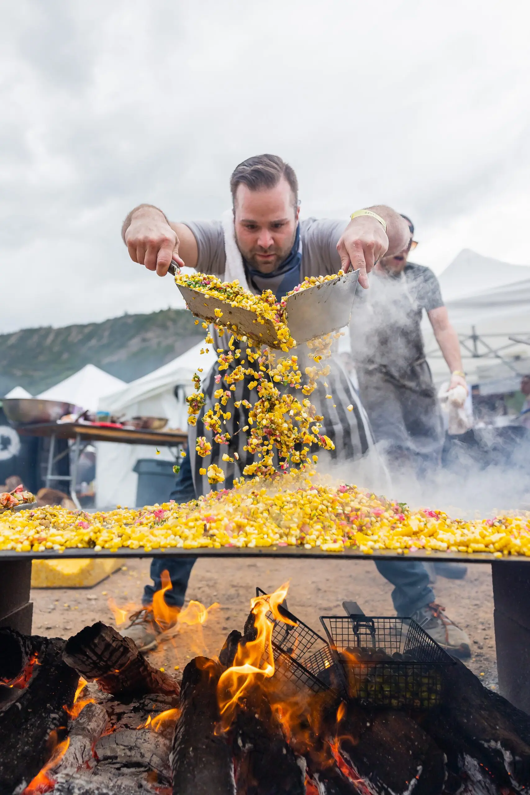 chef mixing and cooking corn over a fire during an outdoors summer event in Aspen Colorado