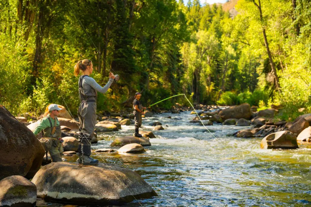 two people standing on the edge of a river and fishing