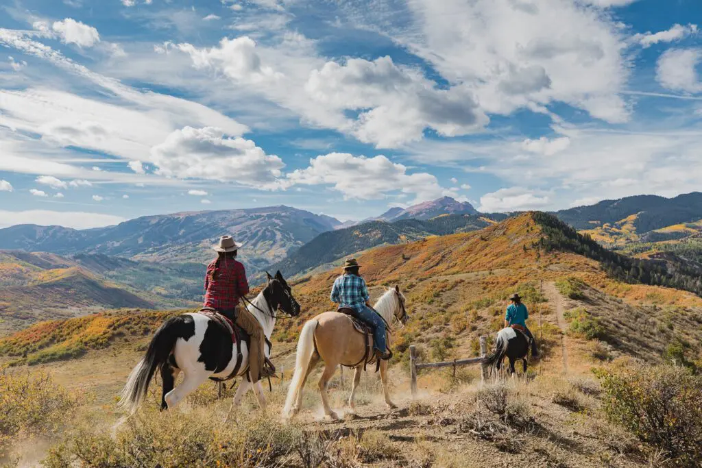 group of people riding horses through the mountains near Aspen Colorado on a crisp fall day with blue sky and wispy white clouds above