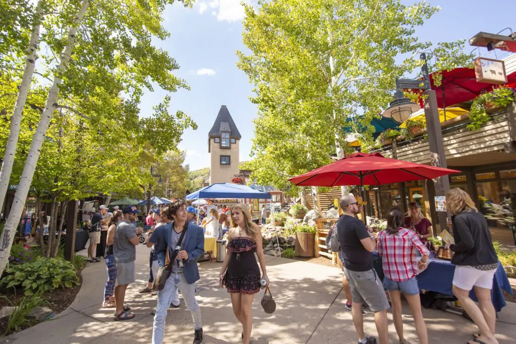 people walking around an outdoor shopping mall area with aspen trees towering toward the sky
