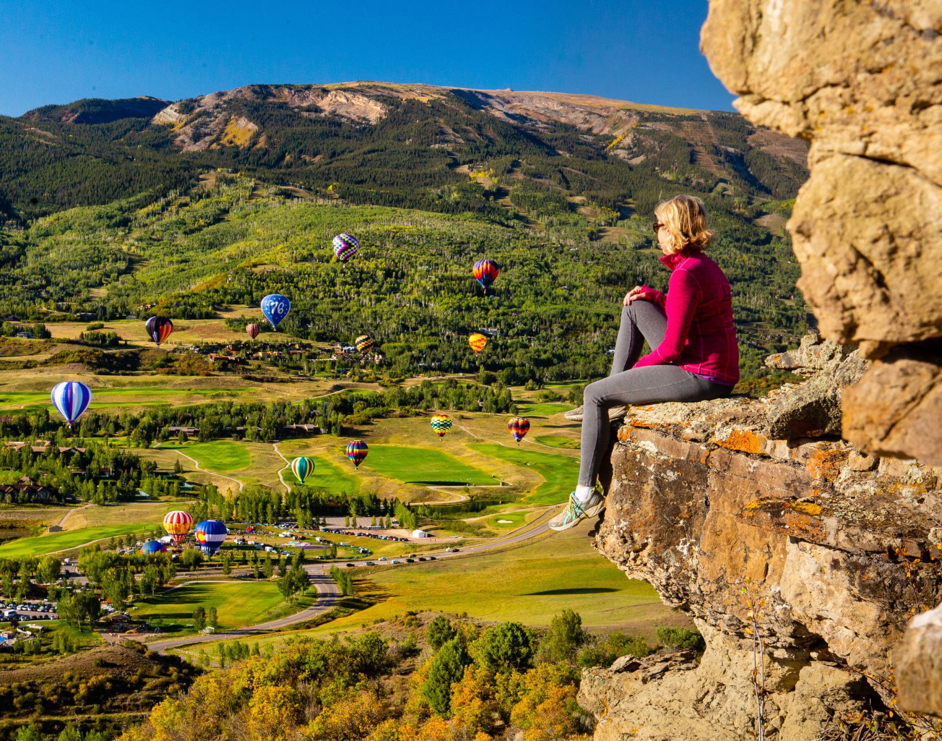 Woman watching hot air balloons from side of cliff