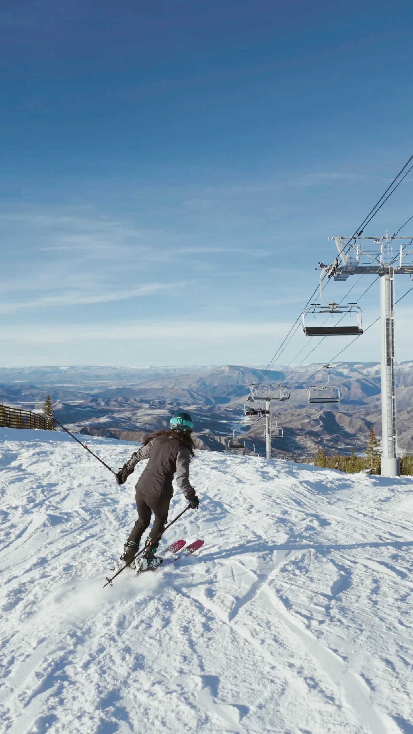 Woman in snowsuit skis down Snowmass Ski Area on a bluebird winter day.