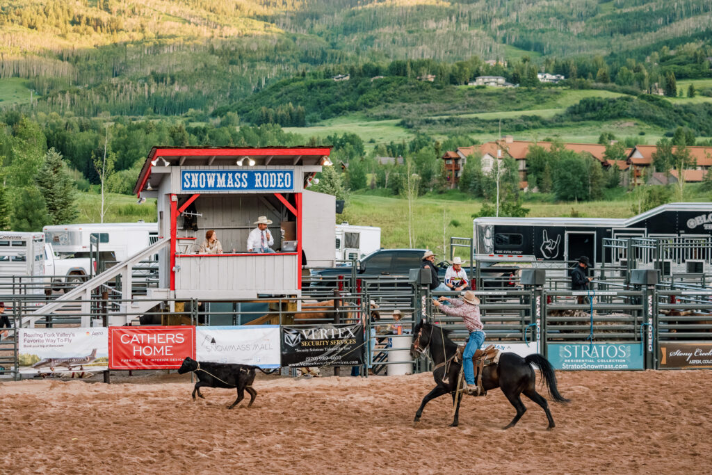 Snowmass Rodeo emcee box, with cowboy on a brown horse wrangling a calf at the Snowmass Rodeo.